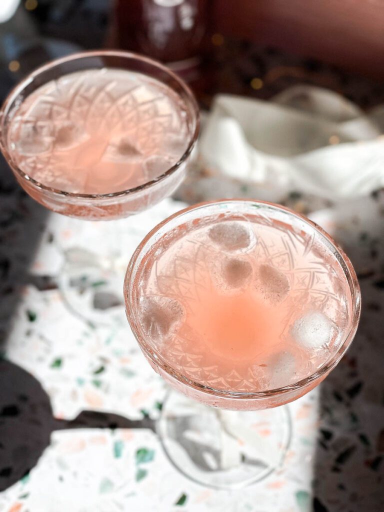 Two stem crystal glasses filled with pink grapefruit and gin sparkling cocktail. 
