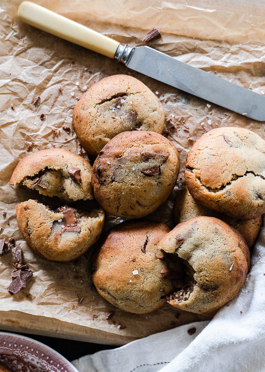Bunch of freshly cooked chocolate chip cookies on a wooden cutting board with butter knife