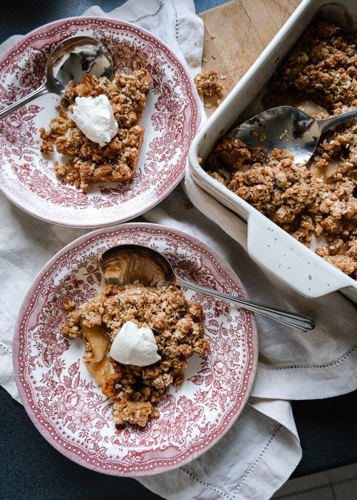 two bowls of warm apple crumble with vanilla ice cream sitting on a wooden chopping board