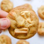 Close up of cookie showing the white chocolate and macadamia nuts. Cookies are seen in the background on a white marble benchtop.
