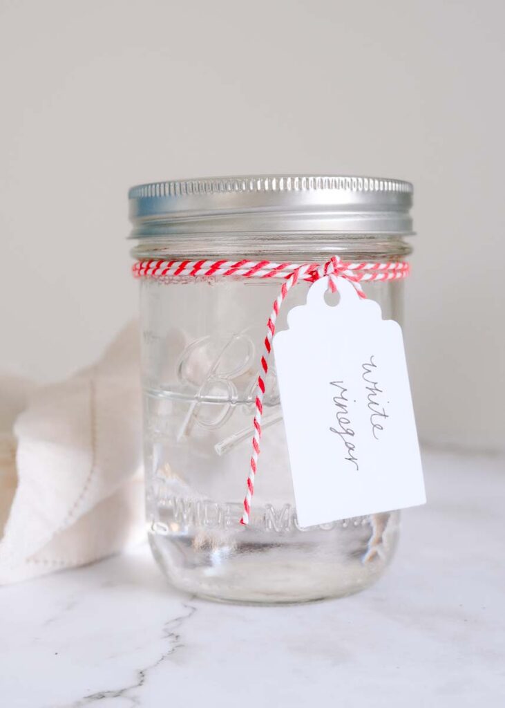 White vinegar stored in a glass mason jar with white label tag tied around jar lid.