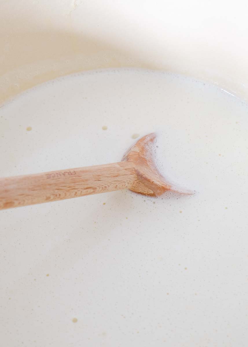 Dutch oven filled with cream and milk being stirred by a wooden spoon