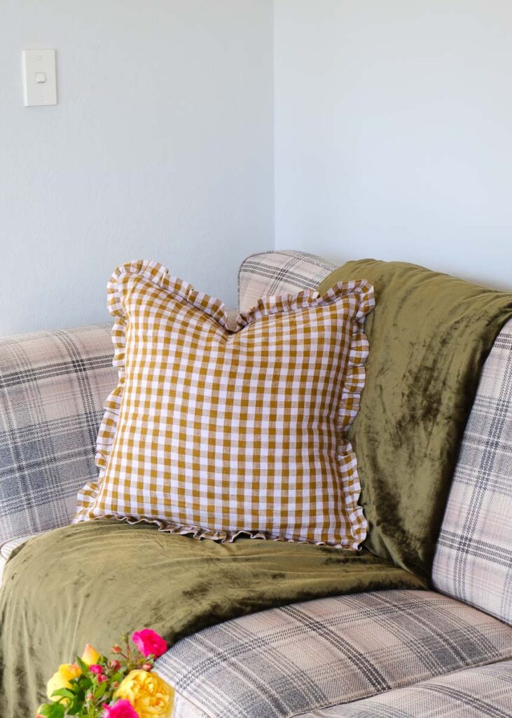 Square cushion with ruffles around the edge on couch made from Merchant and mills  check brown and purple fabric. 