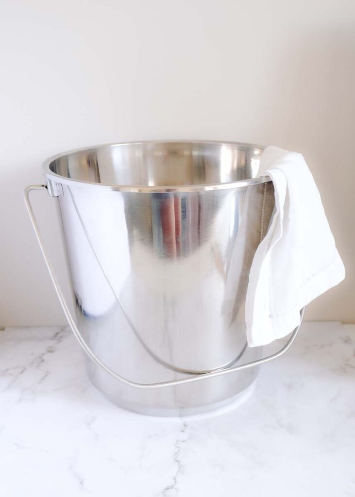 Stainless steel cleaning bucket with linen rag drapped over the side