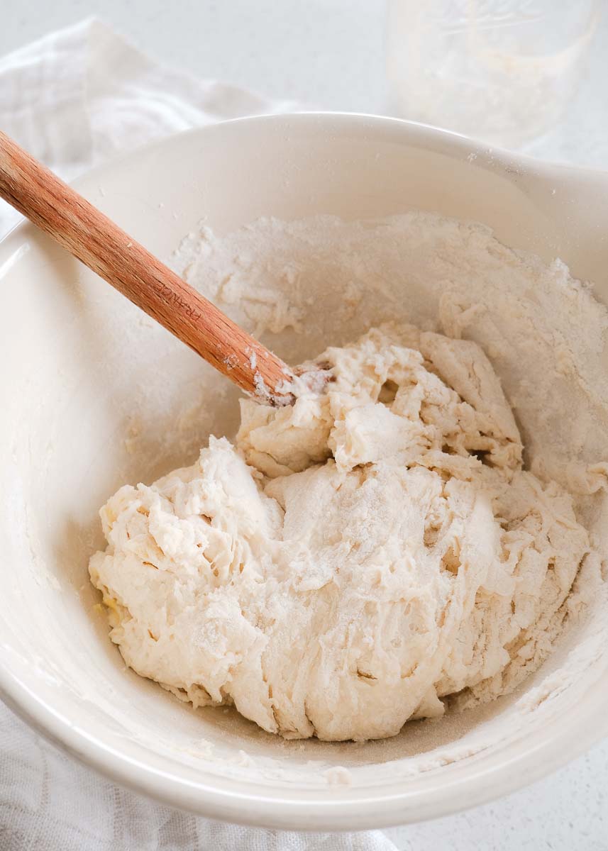 Bread dough being mixed together with wooden spoon in large bowl