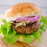 Homemade burger patty in brioche bun with lettuce, red onion and cheese.