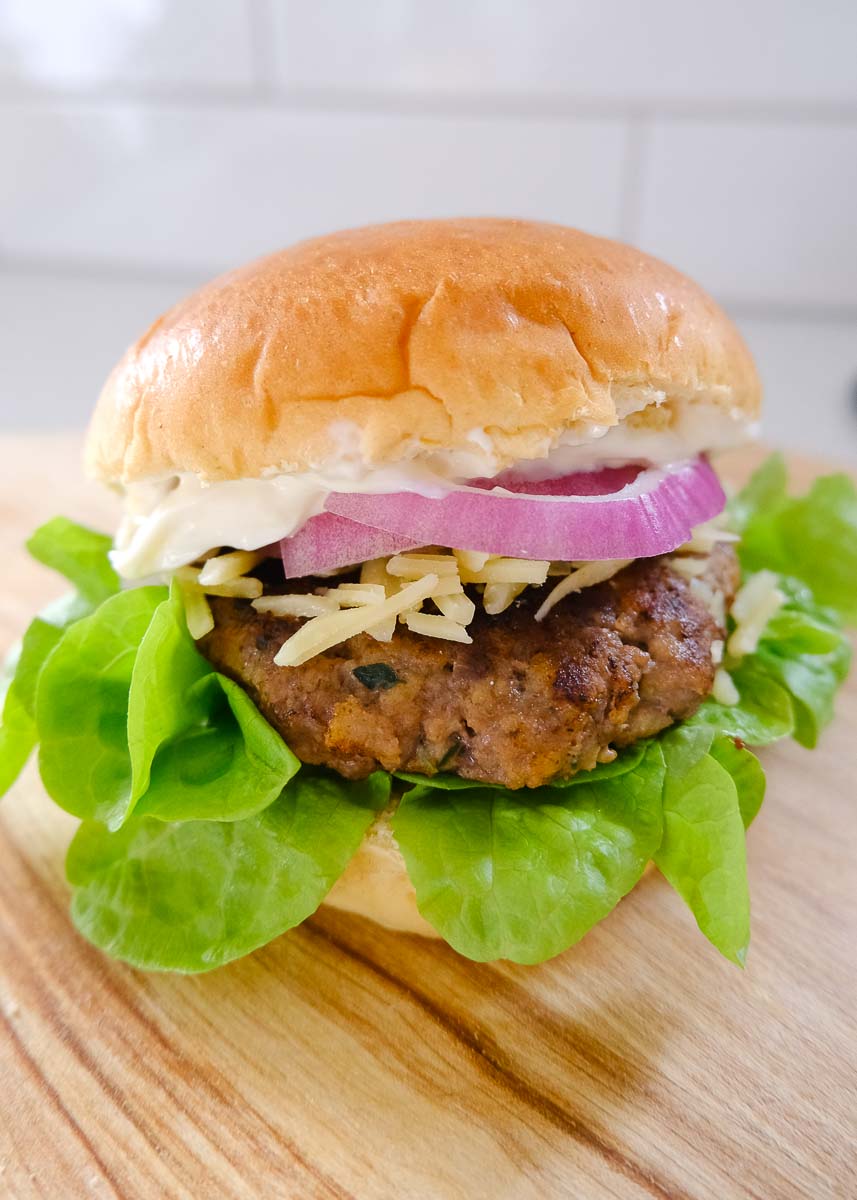 Homemade burger patty in brioche bun with lettuce, red onion and cheese.