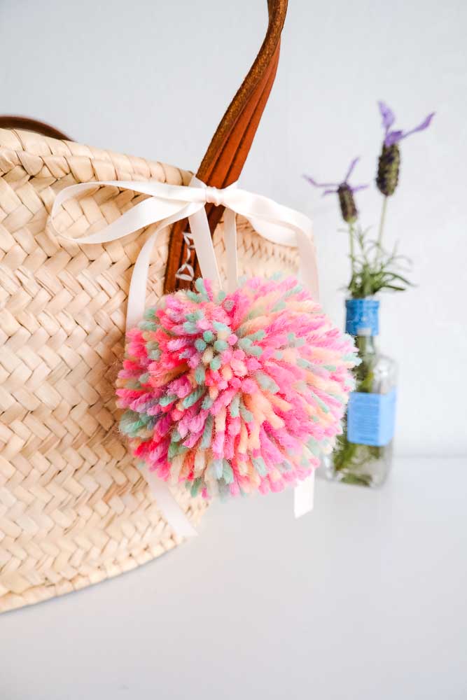 Colourful yarn pom pom hanging on a basket by a white silk ribbon