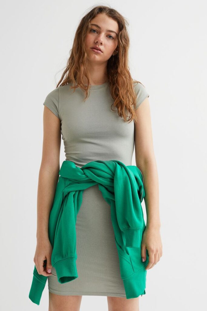 Girl wearing a tight tshirt style cap sleeve dress with a green jumper tied around her waist