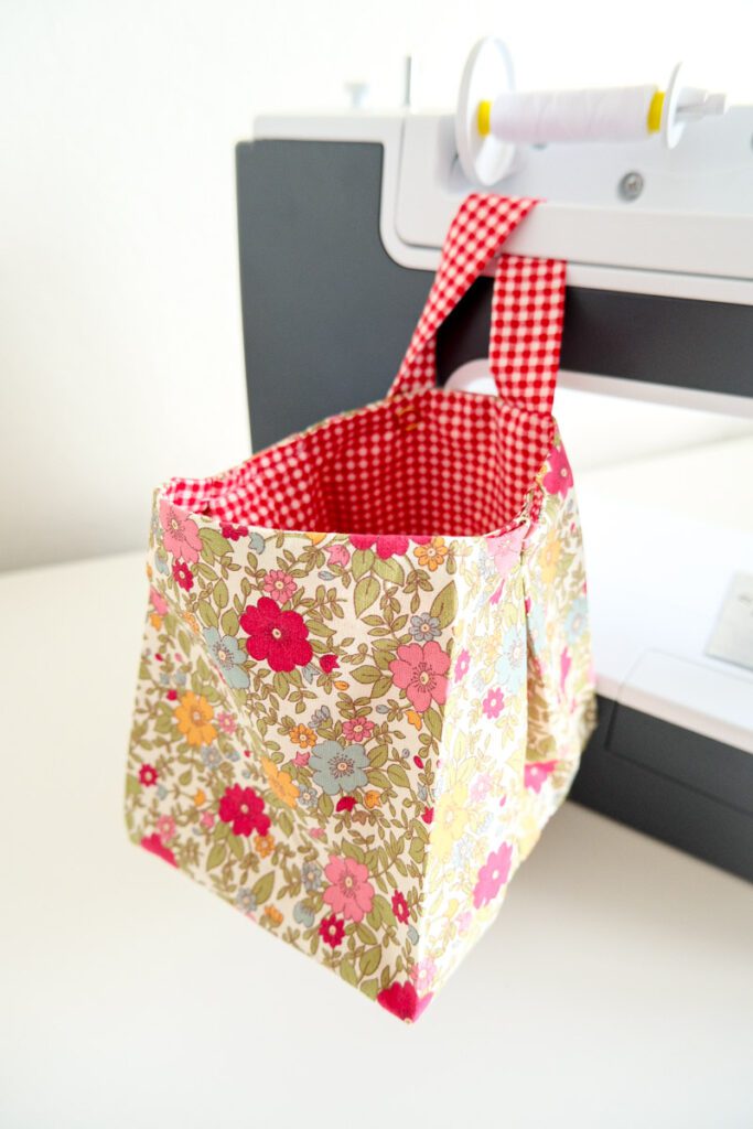 Red and pink floral fabric trash can hanging from Makyla's sewing machine handle