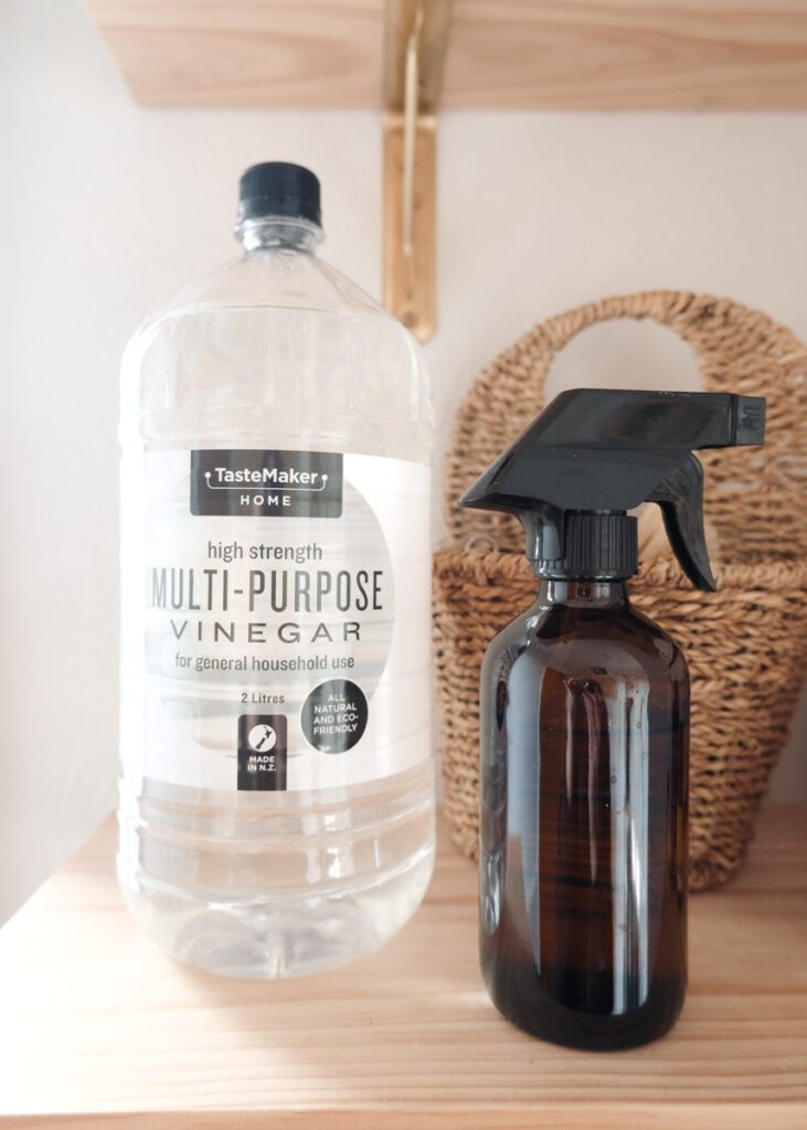 Bottle of cleaning vinegar and amber glass spray bottle on a shelf.