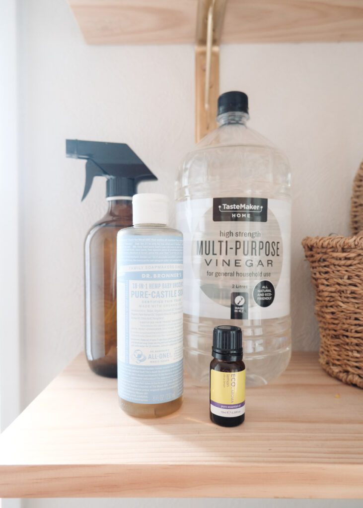 Pure Castile soap, lemon essential oils, cleaning vinegar and a glass amber spray bottle on a wooden shelf