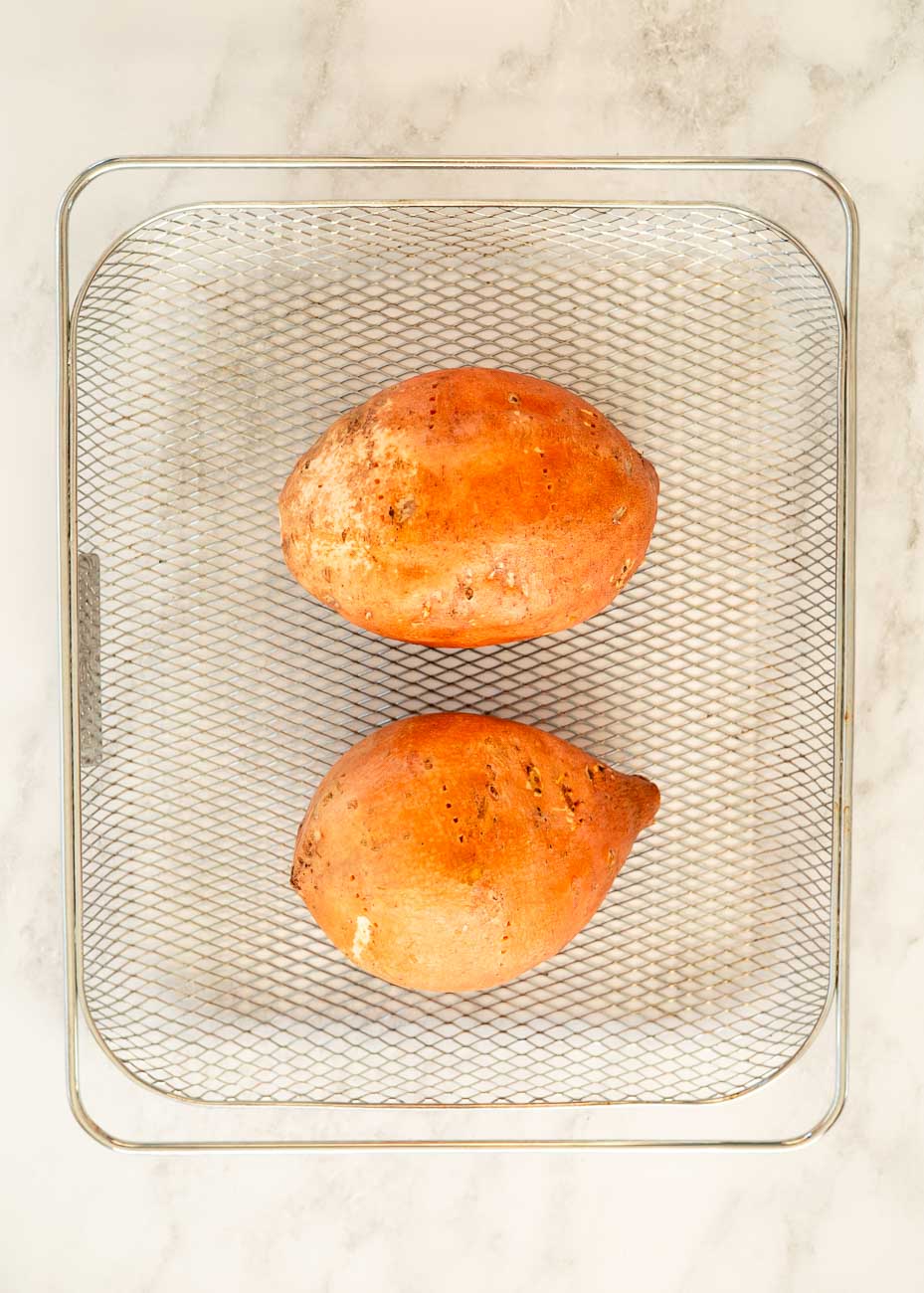 Air fryer basket with pierced sweet potatoes