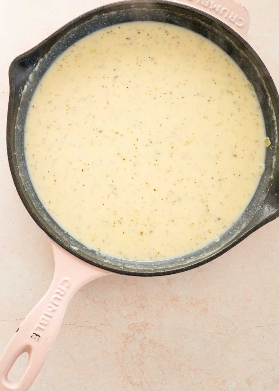 Smooth creamy sauce in a pink-handled skillet, ready for the chicken and vegetables to be added.