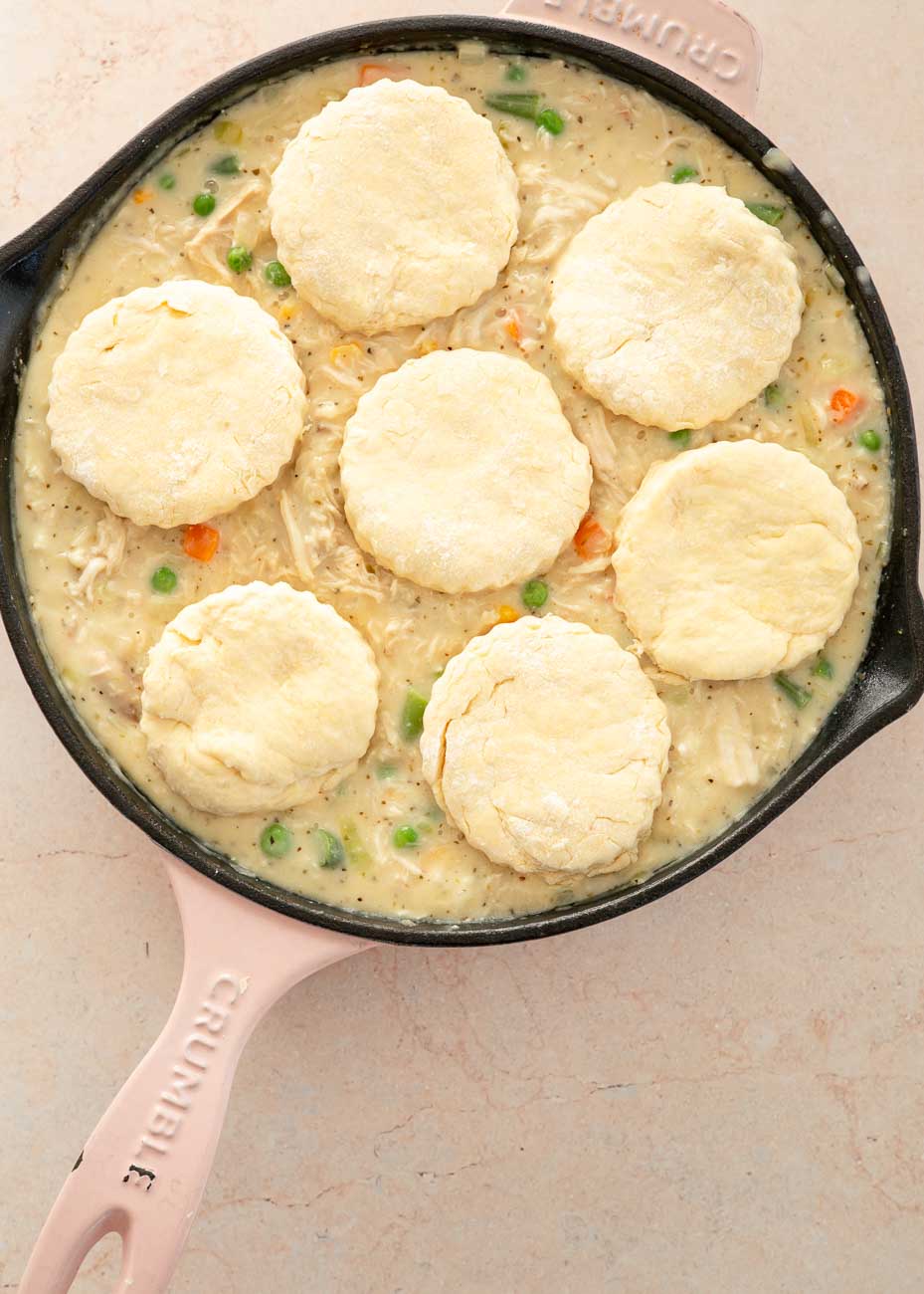 Unbaked biscuits arranged on top of the chicken pot pie filling in the skillet, ready for the oven.