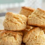 Stack of fluffy, golden old-fashioned buttermilk biscuits on a wooden board.