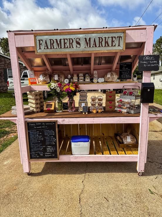 Pink farmer&rsquo;s market stand with eggs, baked goods, flowers, and chalkboard menu