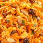 Close-up shot of the mixed carrot salad, showing shredded carrots, raisins, almonds, and pineapple chunks coated in the dressing.