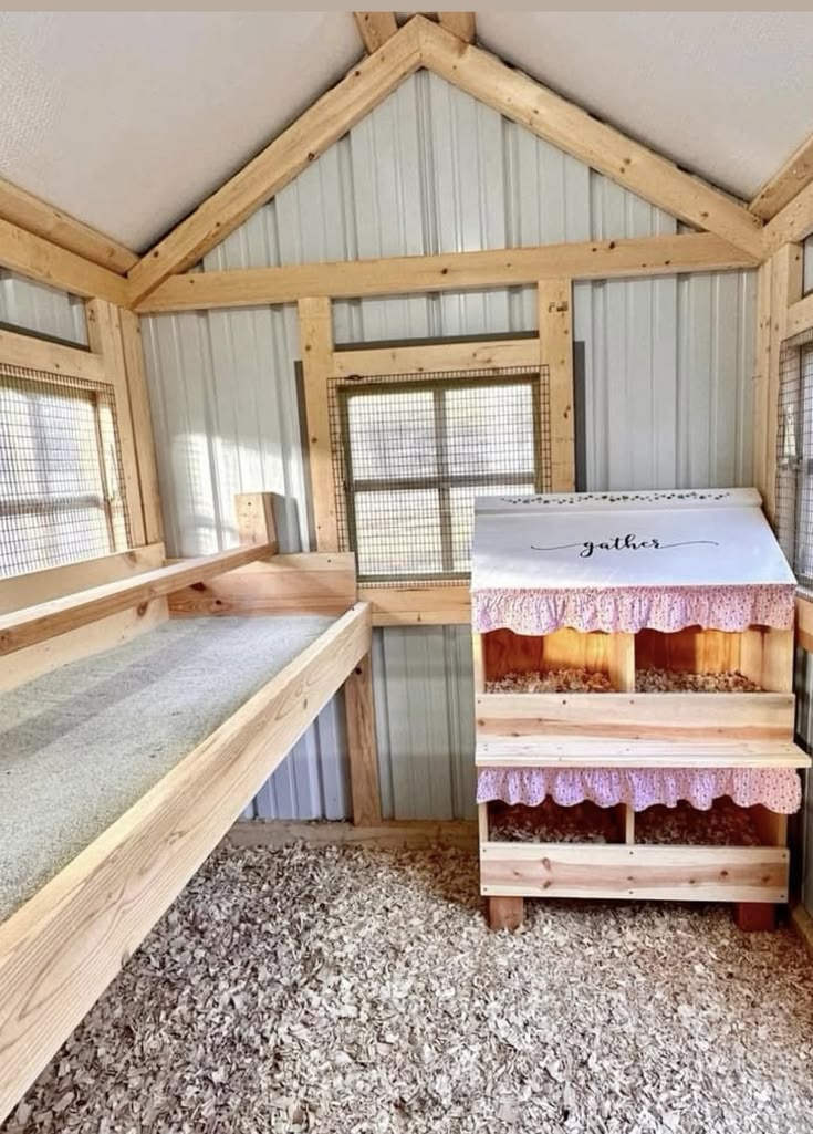 Rustic chicken coop interior with galvanised corrugated metal wall panels, natural timber framing, wide roosting platform along the left wall, and a freestanding cedar nesting box with pink gathered fabric trim, ruffle detail around nest entries, and a handwritten gather sign on the lid.