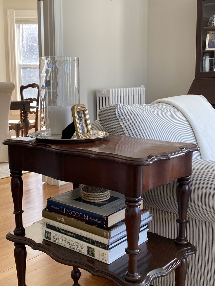Wooden side table with turned legs styled with a glass hurricane candle holder on a silver tray and a small gold photo frame, striped sofa cushion beside it