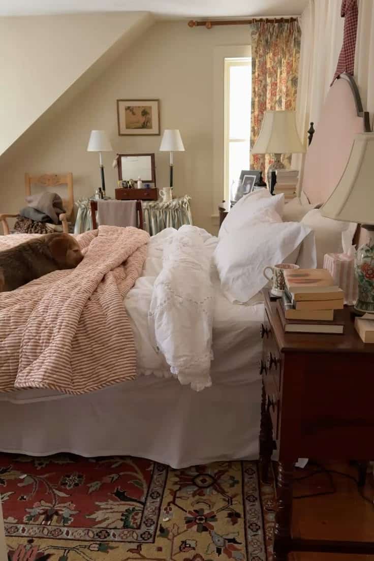 Cottagecore bedroom with warm floral curtains, a Persian-style rug on the floor, layered white and terracotta linen bedding, matching tall bedside lamps, and a ruffled dressing table skirt