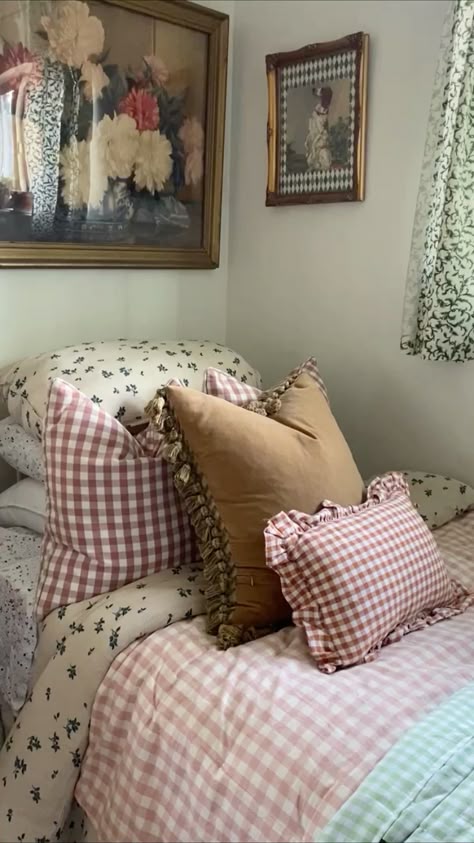 Cottagecore bedroom bed styled with pink gingham cushions, a caramel velvet pillow with tassel trim, ruffled gingham accent cushion, floral bedding, and vintage framed artwork above the headboard