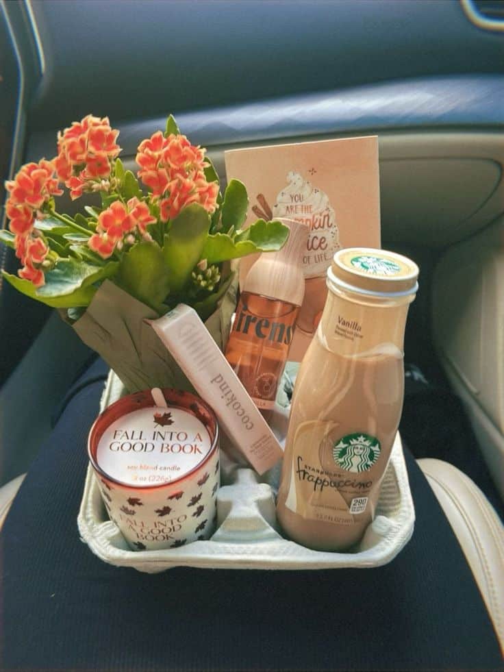 Car cup holder tray with a Fall Into A Good Book soy candle, Starbucks vanilla Frappuccino bottle, lip balm, Sirens hair and body mist, autumn greeting card, and a potted orange kalanchoe plant