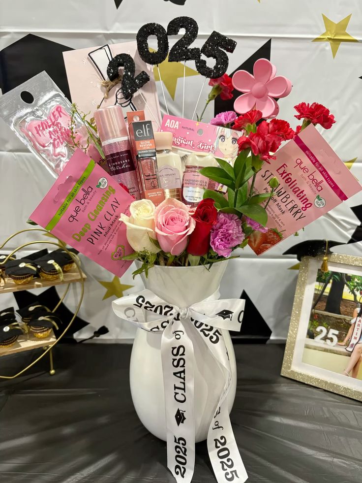 A white vase filled with pink roses, carnations, and beauty products including e.l.f. glow spray, face masks, and lip glosses, tied with a Class of 2025 ribbon
