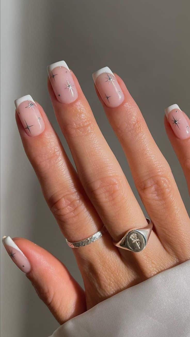Square French tip nails in white with small silver starburst nail art scattered across the nail bed