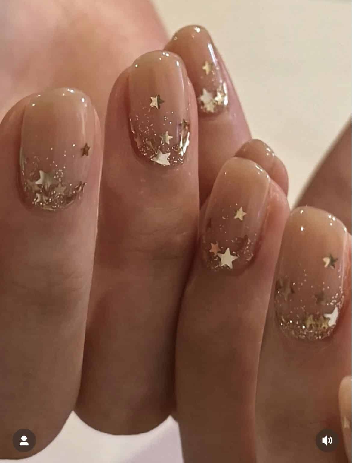 Short rounded nails with a nude base and gold glitter star tips clustered toward the nail edge