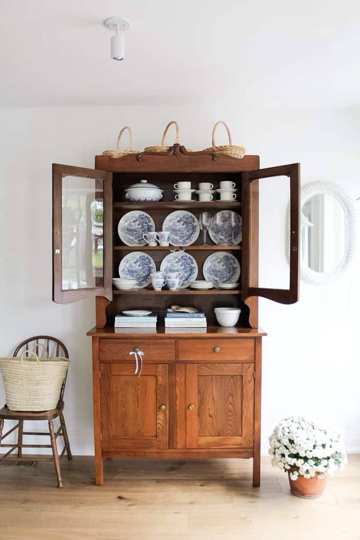 Timber glass-front hutch with doors open displaying blue and white transferware plates bowls and teacups on shelves with stacked books and a white bowl on the surface below