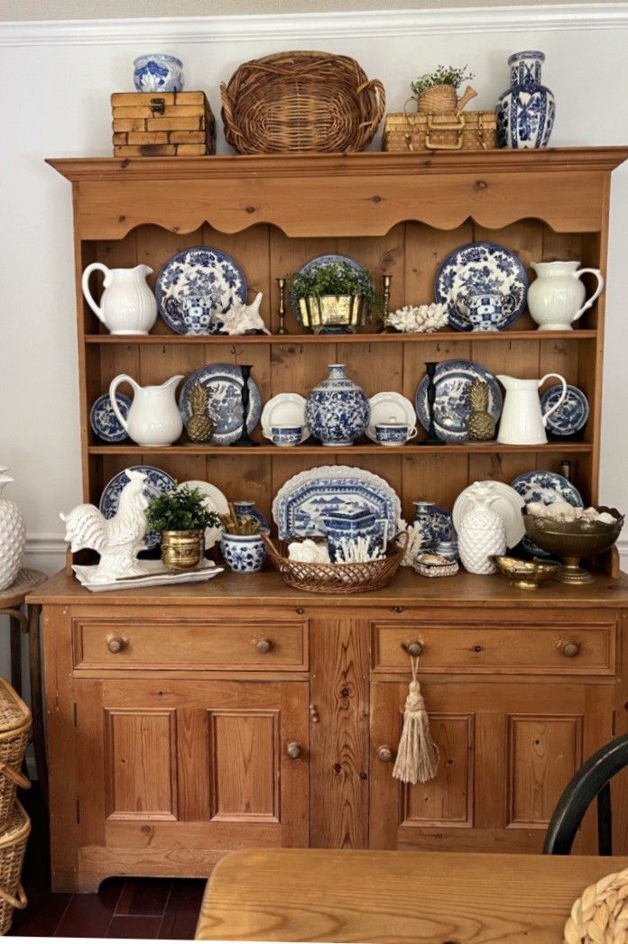 Dark pine hutch with white-painted shelves filled with antique stoneware crocks salt-glazed pottery yellow mixing bowls mason jars and a small framed print