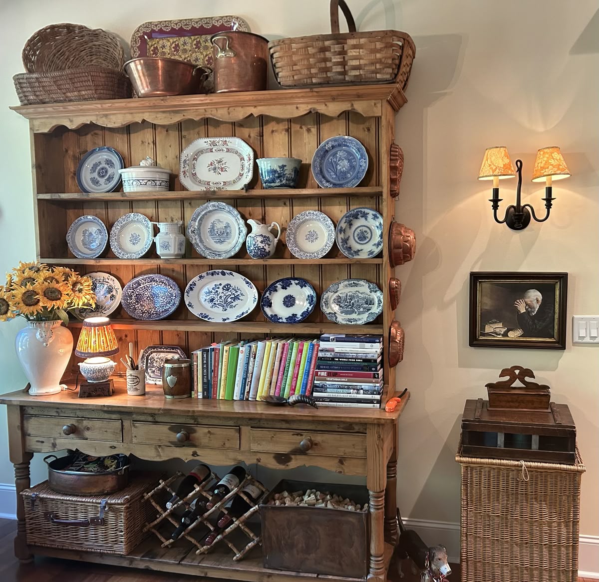 Pine hutch filled with blue and white transferware plates platters and jugs with colourful cookbooks a lamp and copper pots and wicker baskets stacked on top