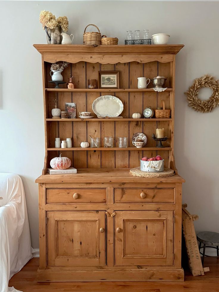 Pine hutch styled for autumn with dried hydrangeas cream pitchers a small pumpkin wicker baskets and vintage ceramics on each shelf