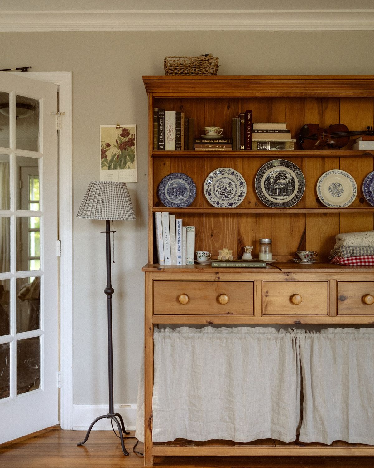 Pine hutch with a linen skirt on the lower section blue and white transferware plates on shelves cookbooks and a violin displayed with small collectibles