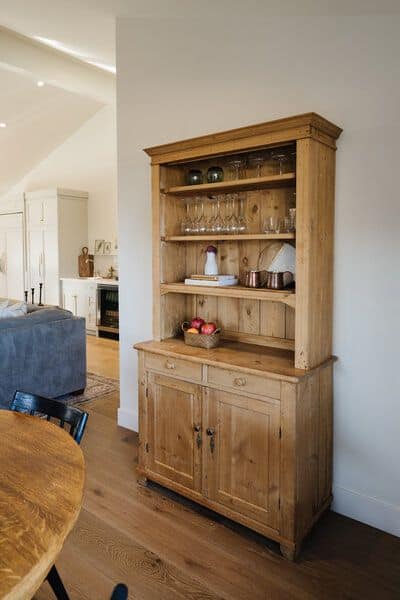 Simple pine hutch with clear and stemmed glassware on upper shelves and a small bowl of red apples on the surface in a modern open plan dining room
