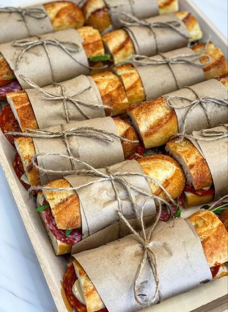 Individual baguette sandwiches wrapped in brown paper and tied with twine arranged in a wooden tray for a Peter Rabbit baby shower food table