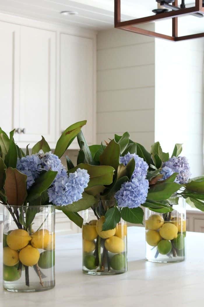 Blue hydrangea and magnolia leaf arrangements in glass cylinder vases with lemons and limes as centrepieces for a Peter Rabbit baby shower table