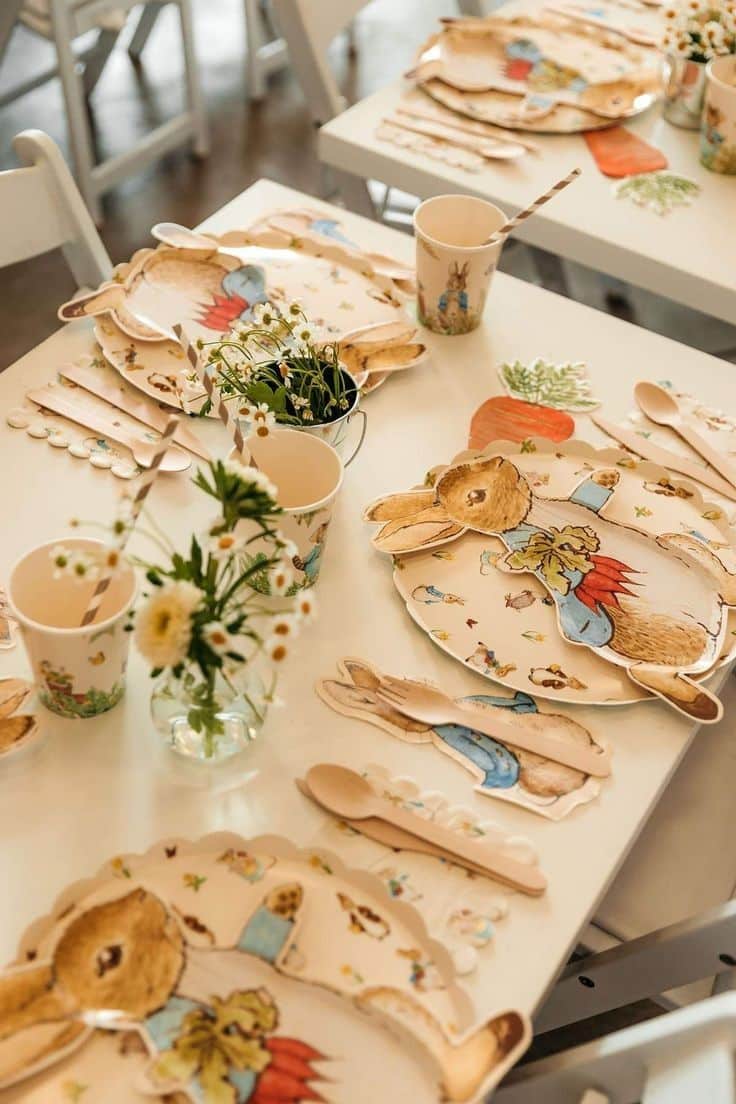 Peter Rabbit baby shower table setting with Meri Meri rabbit shaped plates illustrated cups printed napkins wooden cutlery and small daisy posies in mini metal buckets