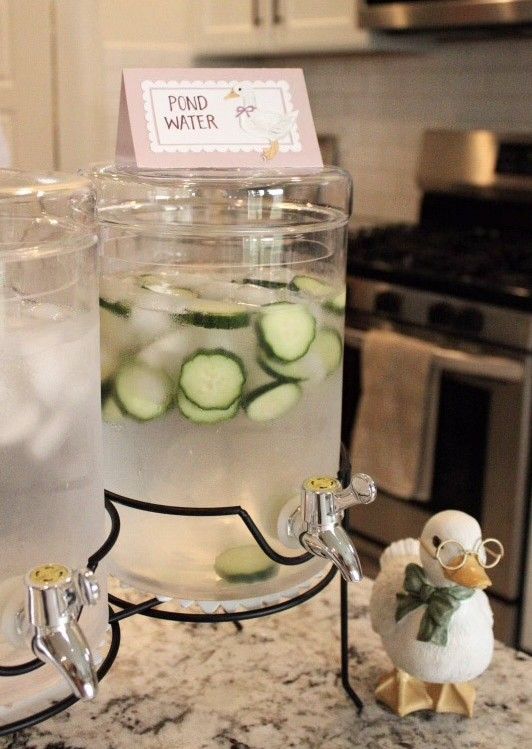 Peter Rabbit baby shower cucumber water dispenser labelled Pond Water with a Jemima Puddle-Duck ceramic figurine beside it on a kitchen counter