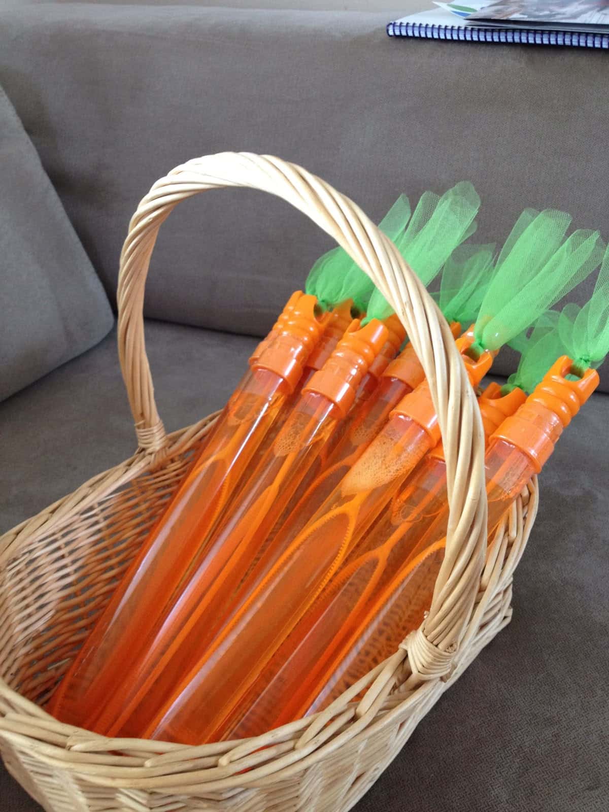 Wicker basket filled with orange carrot shaped bubble wands with green tulle tops as Peter Rabbit baby shower party favours