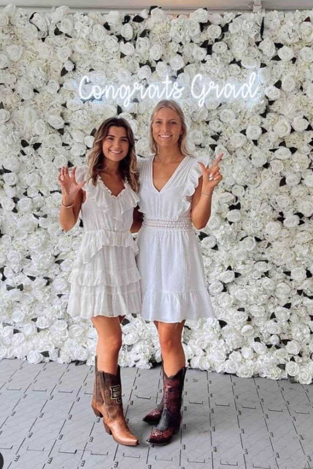 Full backdrop of densely packed white faux roses with a glowing neon sign reading Congrats Grad mounted in the centre