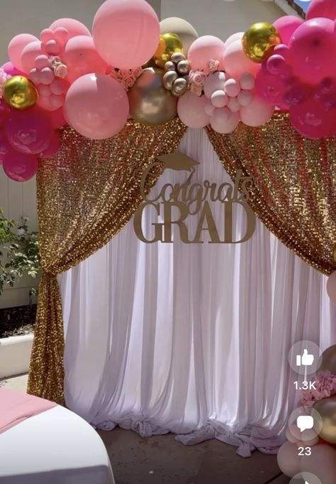Graduation party backdrop with draped gold sequin fabric panels opening to reveal a white curtain backdrop with a Congrats Grad gold sign and pink and gold balloon arch overhead
