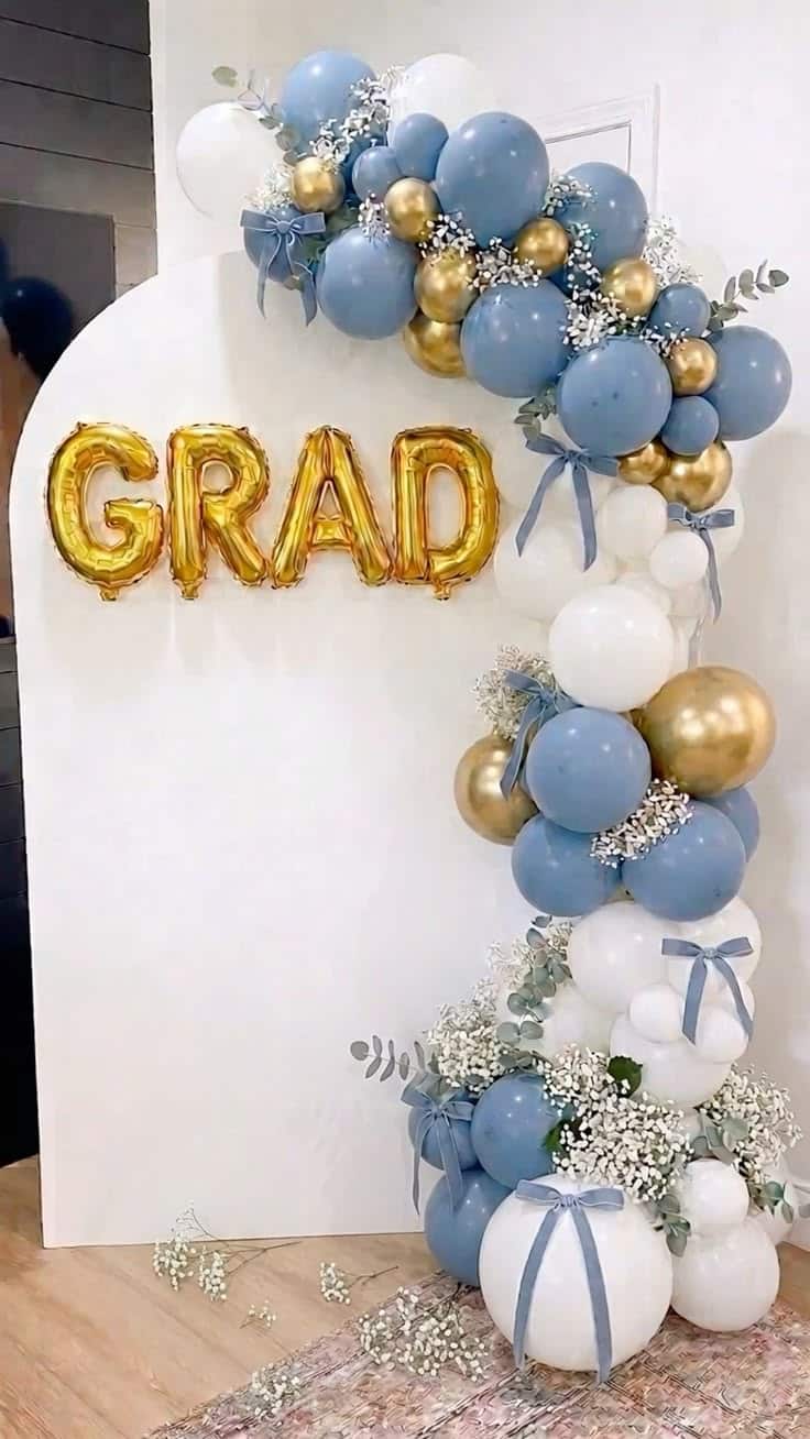 White arched panel backdrop with a dusty blue white and gold balloon garland featuring eucalyptus sprigs baby's breath and small blue ribbon bows