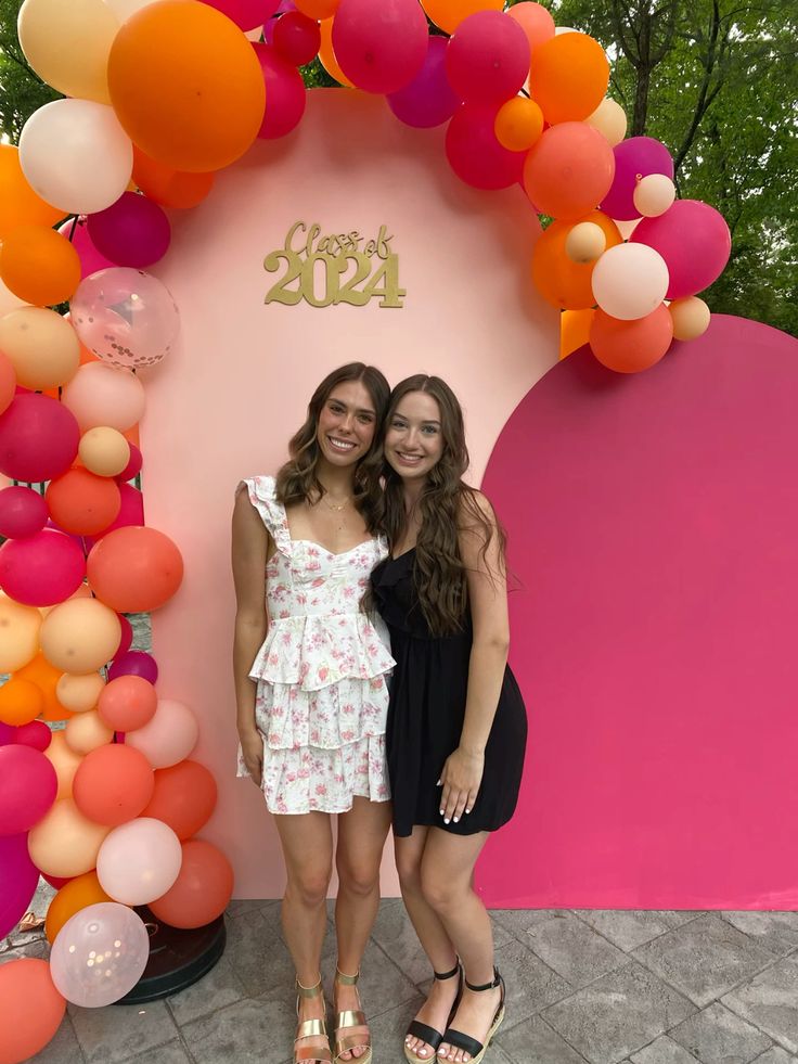 Two-tone graduation arch panel in blush pink and hot fuchsia with a vibrant orange pink and peach balloon garland and a gold Class of 2024 sign