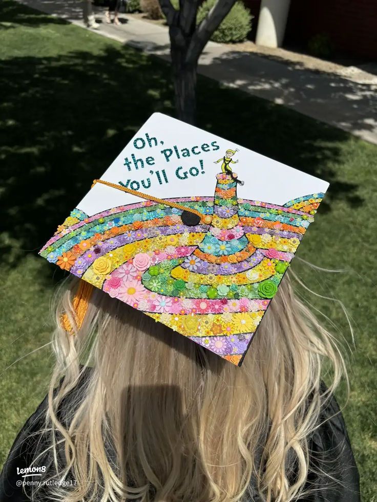 White graduation cap with a Dr Seuss illustration and the words oh the places you'll go, with the lower half covered in concentric rings made entirely from tiny colourful paper flowers.
