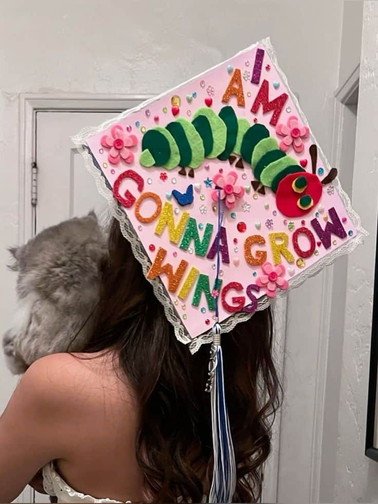 Pink graduation cap with a felt Very Hungry Caterpillar and glitter letter stickers spelling out I am gonna grow wings.