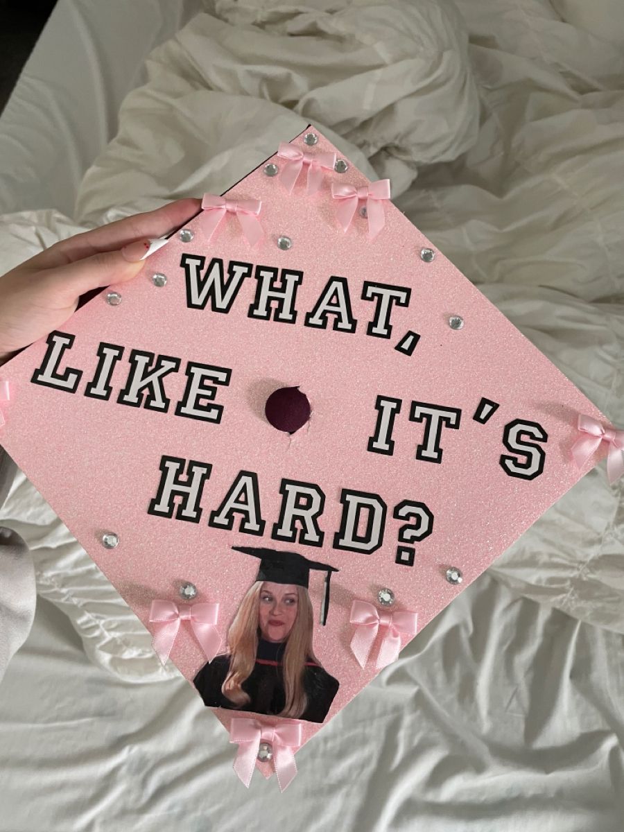 Pink glitter graduation cap with white and black varsity letters reading what like it's hard, pink satin bows at each corner, rhinestones, and a photo of Elle Woods from Legally Blonde.