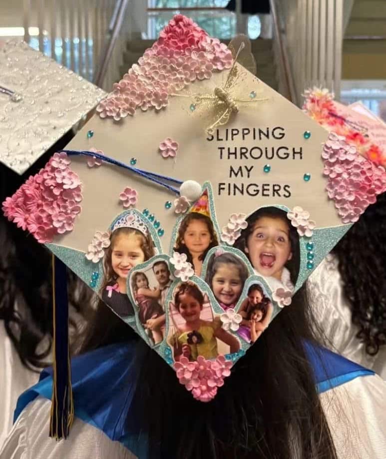 White graduation cap with pink hydrangea flowers, rhinestones, a golden bow, and a collage of childhood photos surrounded by small paper flowers.