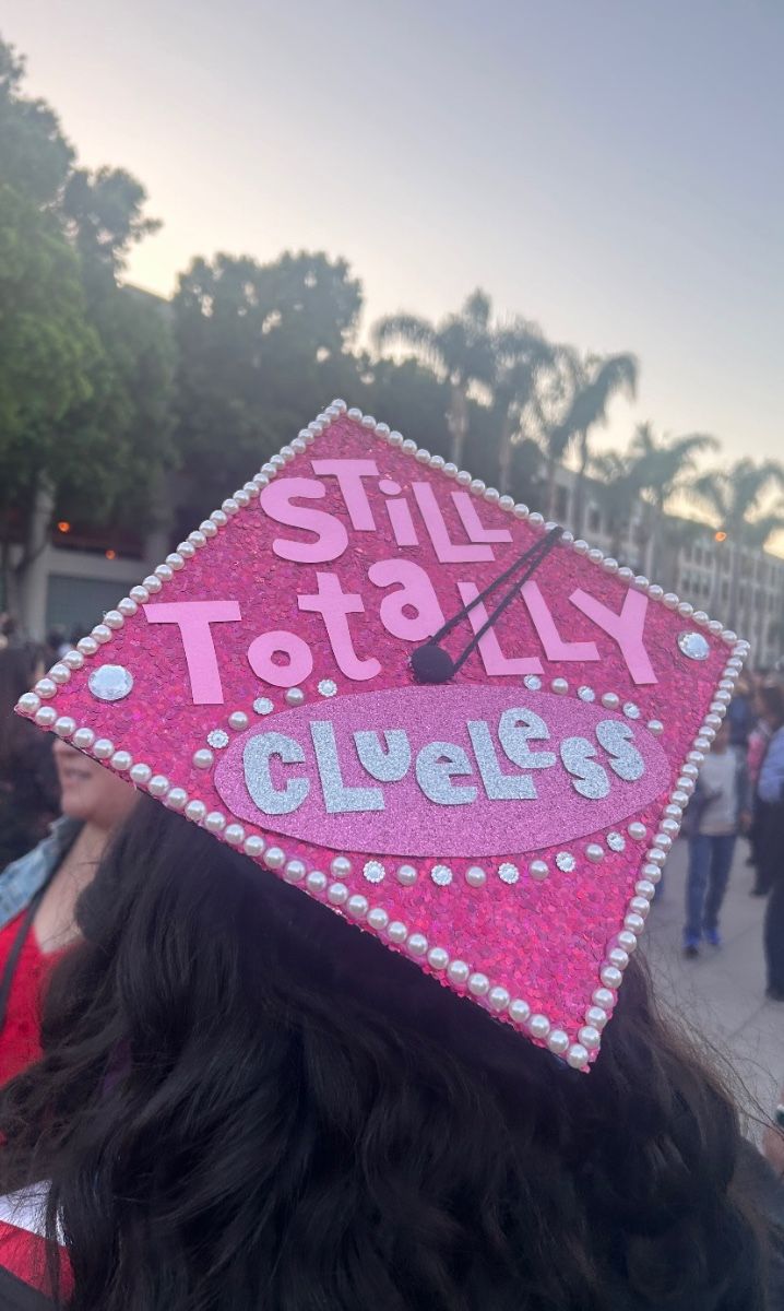 Hot pink glitter graduation cap with pearl border and the words still totally clueless in mixed pink and silver lettering.